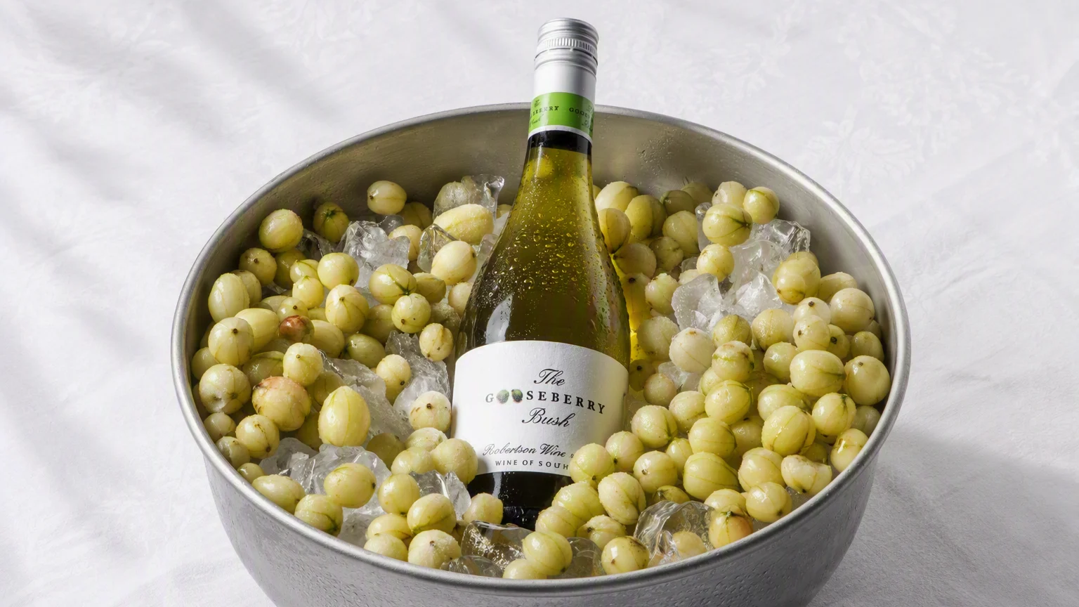 Bottle of Gooseberry Bush Sauvignon Blanc chilling in ice alongside fresh gooseberries.
