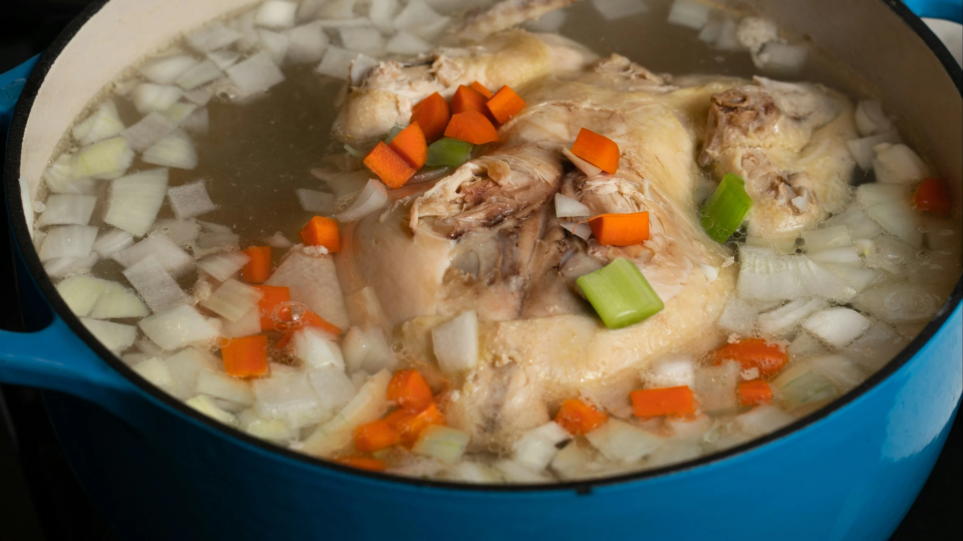 Whole chicken simmering in a stockpot with chopped onion, carrot and celery for homemade stock.
