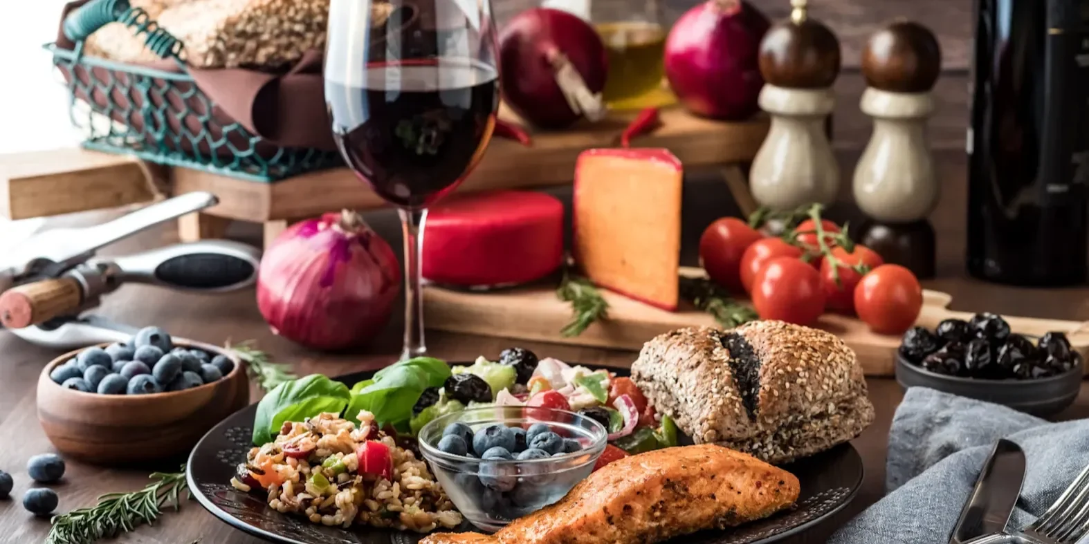 Plate with cooked salmon, grains, salad, and blueberries beside a glass of red wine.
