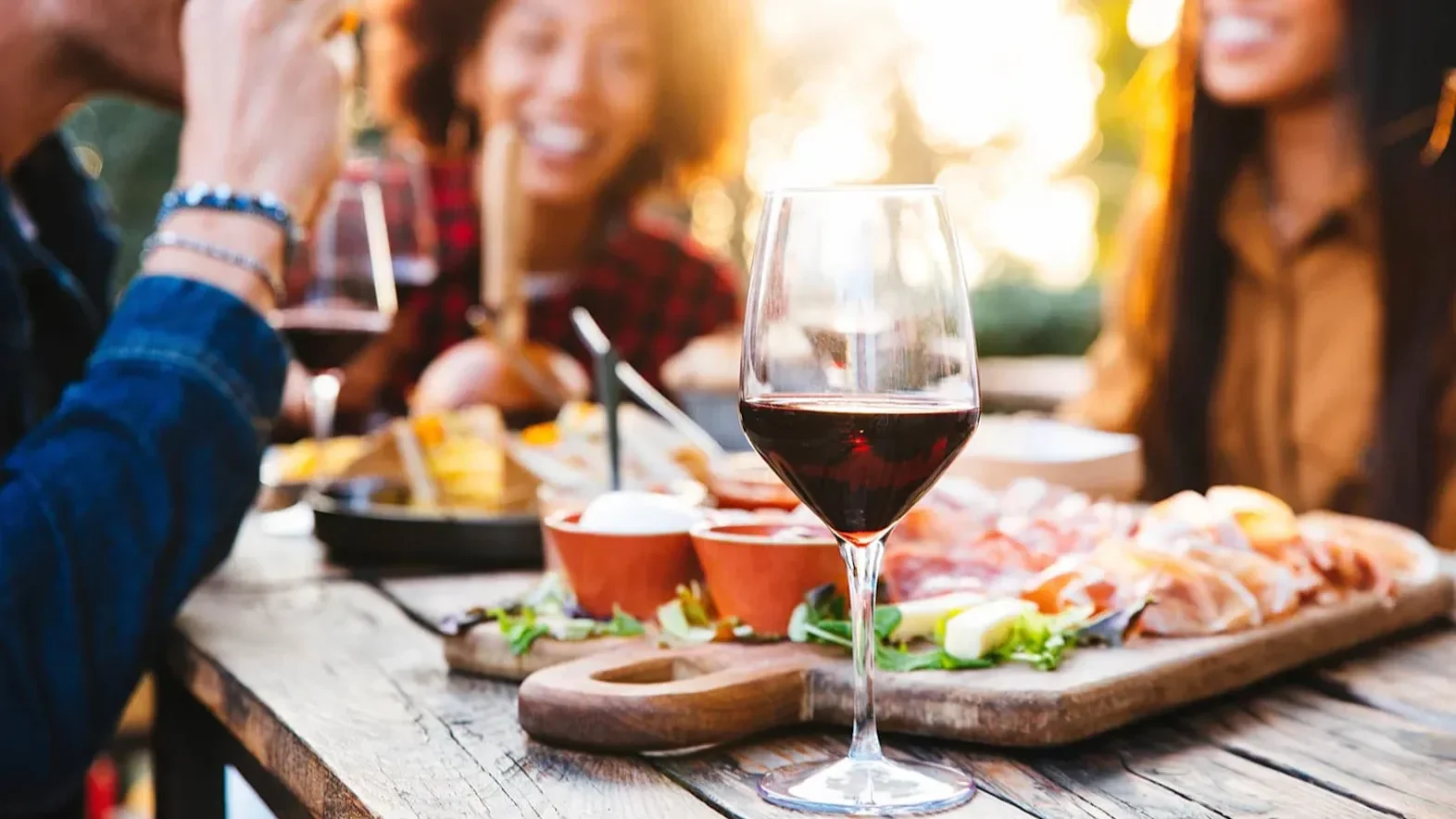 Glass of red wine on a wooden table with shared food platters during an outdoor meal.