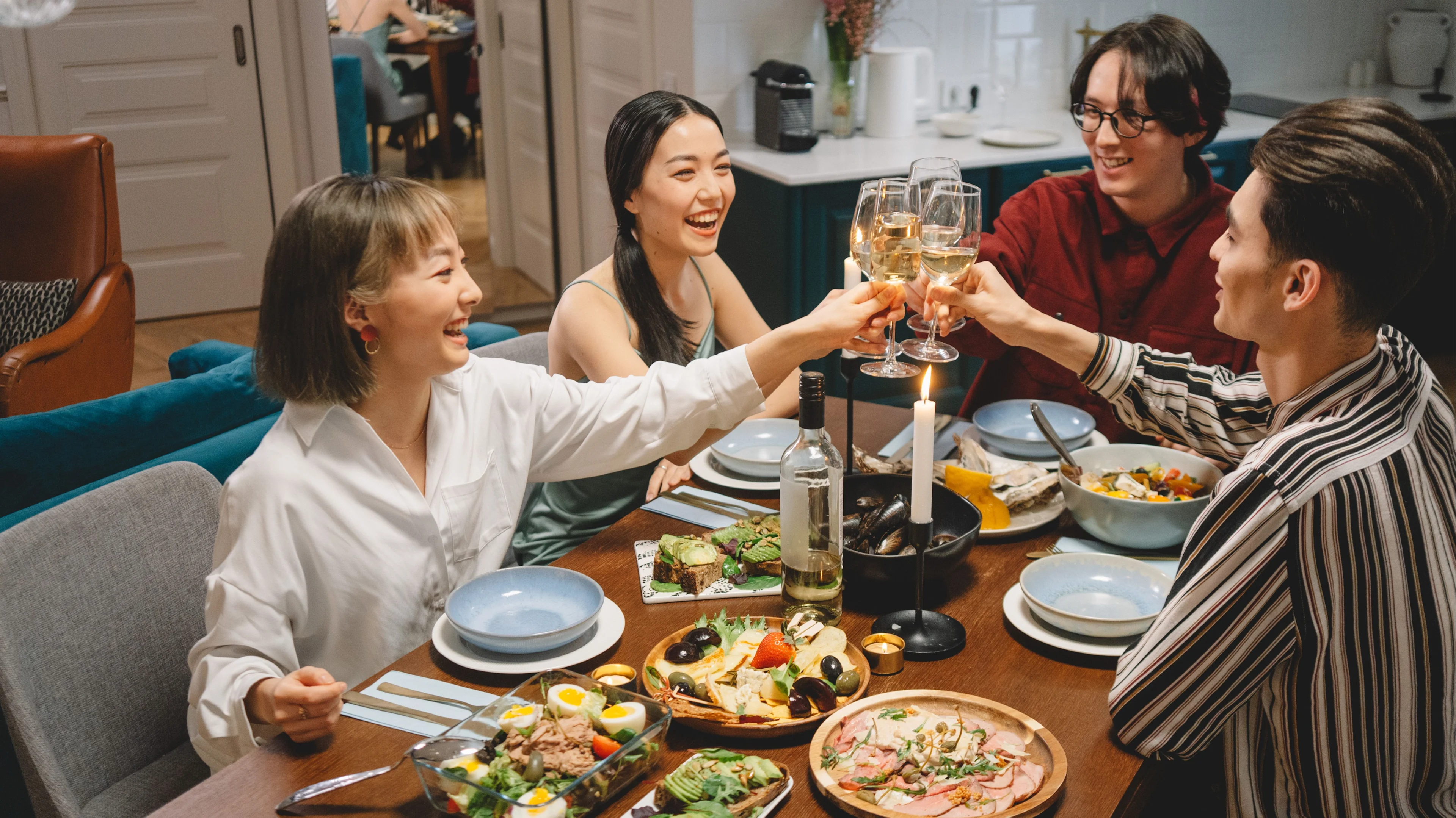 People raising glasses of white wine around a dining table filled with shared dishes and candles.