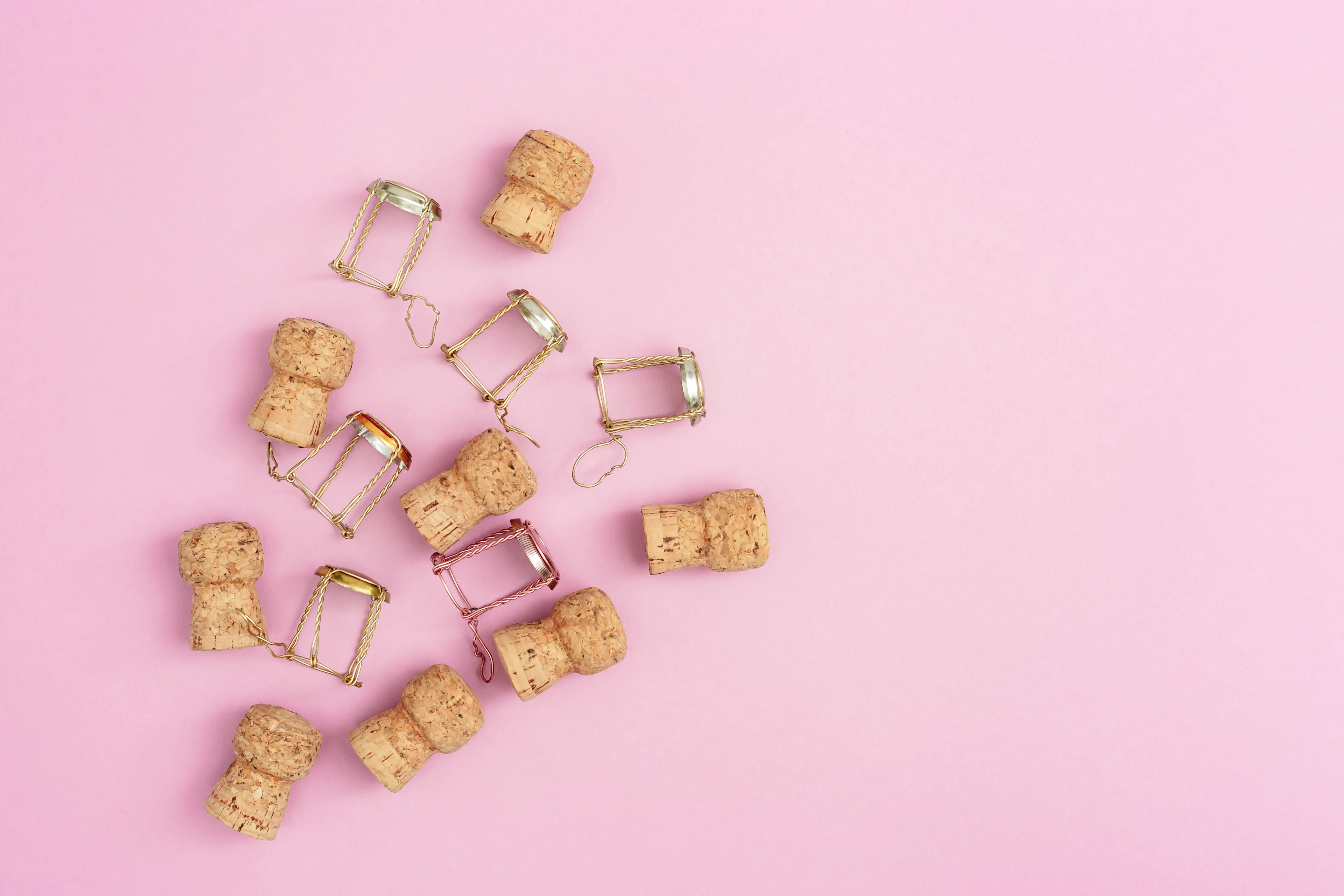 Champagne corks and wire cages scattered on a pink background.