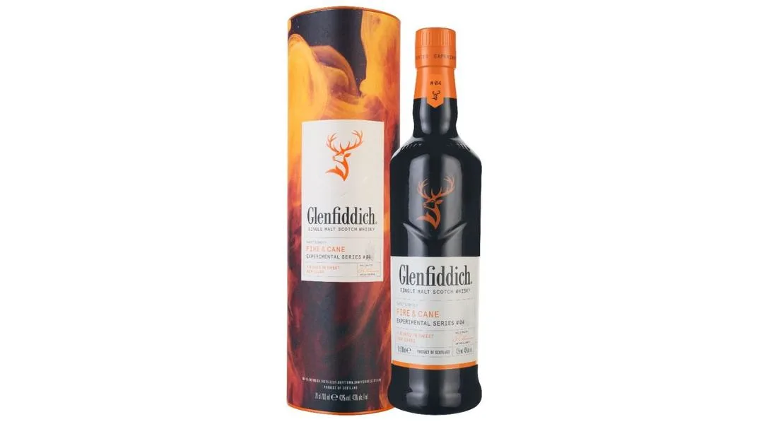 A bottle of Glenfiddich Fire & Cane Experimental Series single malt Scotch whisky with an orange cap, placed next to its cylindrical box featuring fiery orange and black design, on a white background.