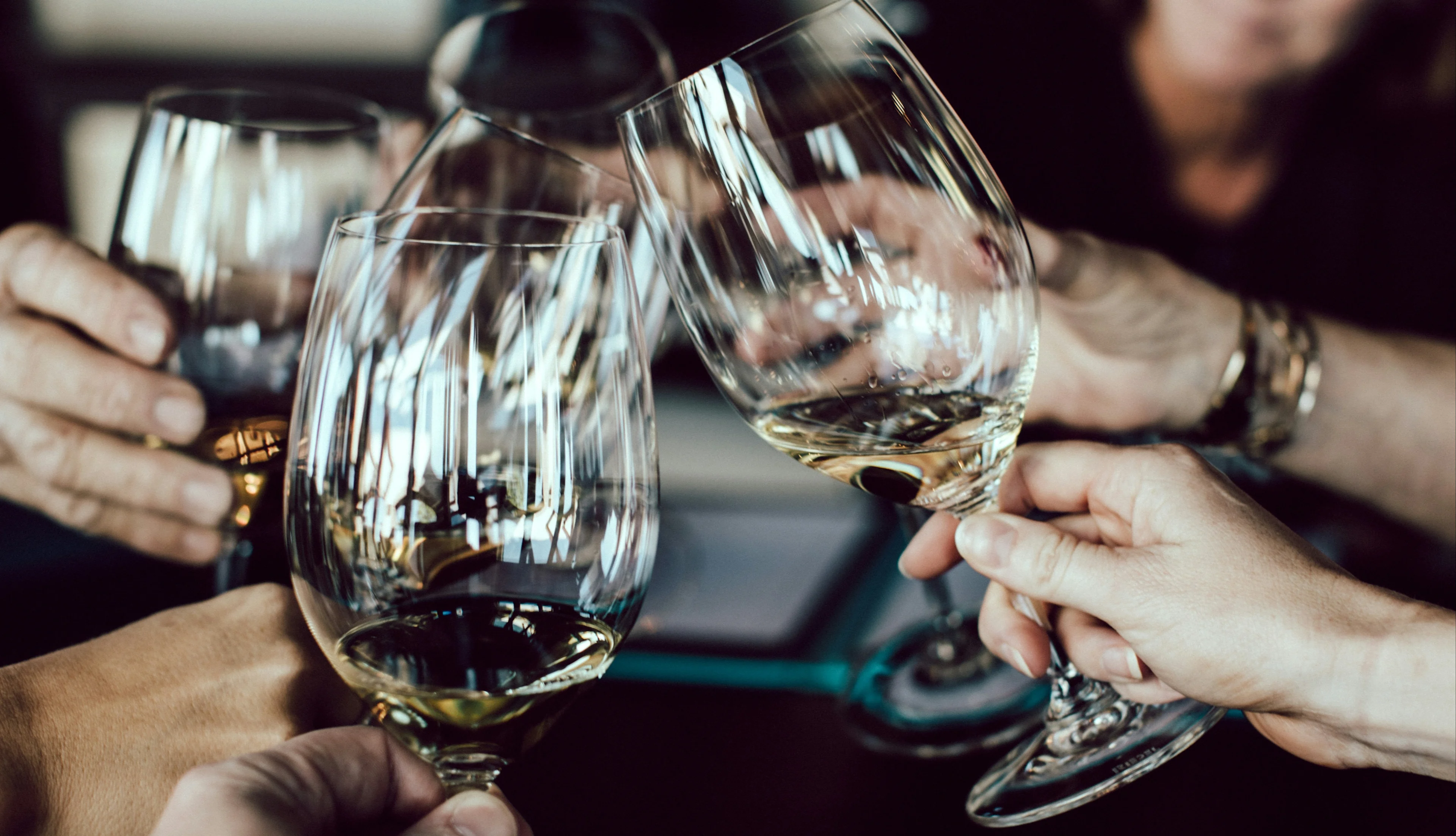 Several people clinking glasses of white and red wine during a wine tasting or shared meal indoors.