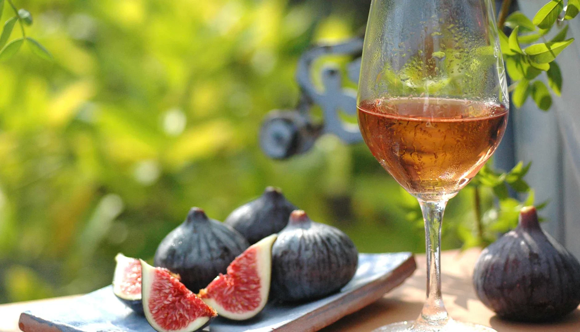 A glass of rose wine outdoors on a table with figs.