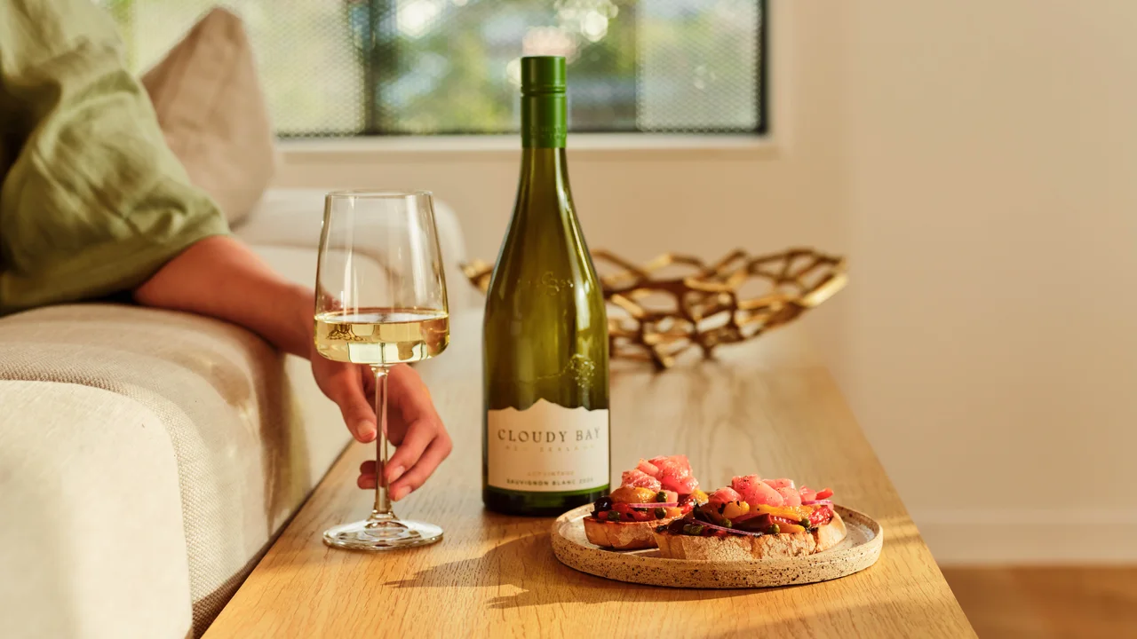 Bottle and glass of Sauvignon Blanc beside tuna bruschetta on a wooden table in a sunlit living room.