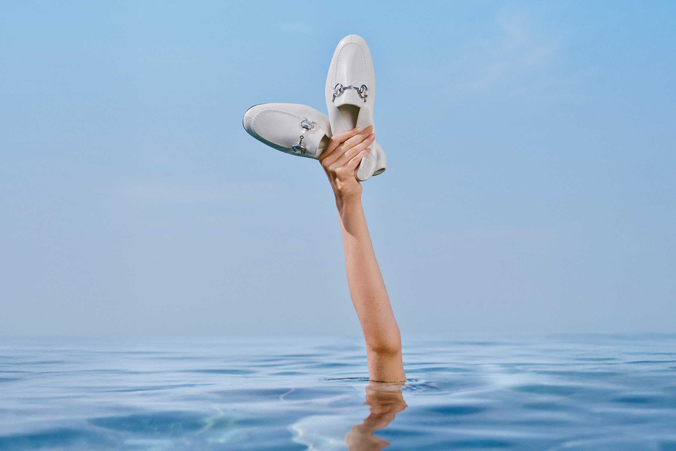White Gucci horsebit loafers held aloft