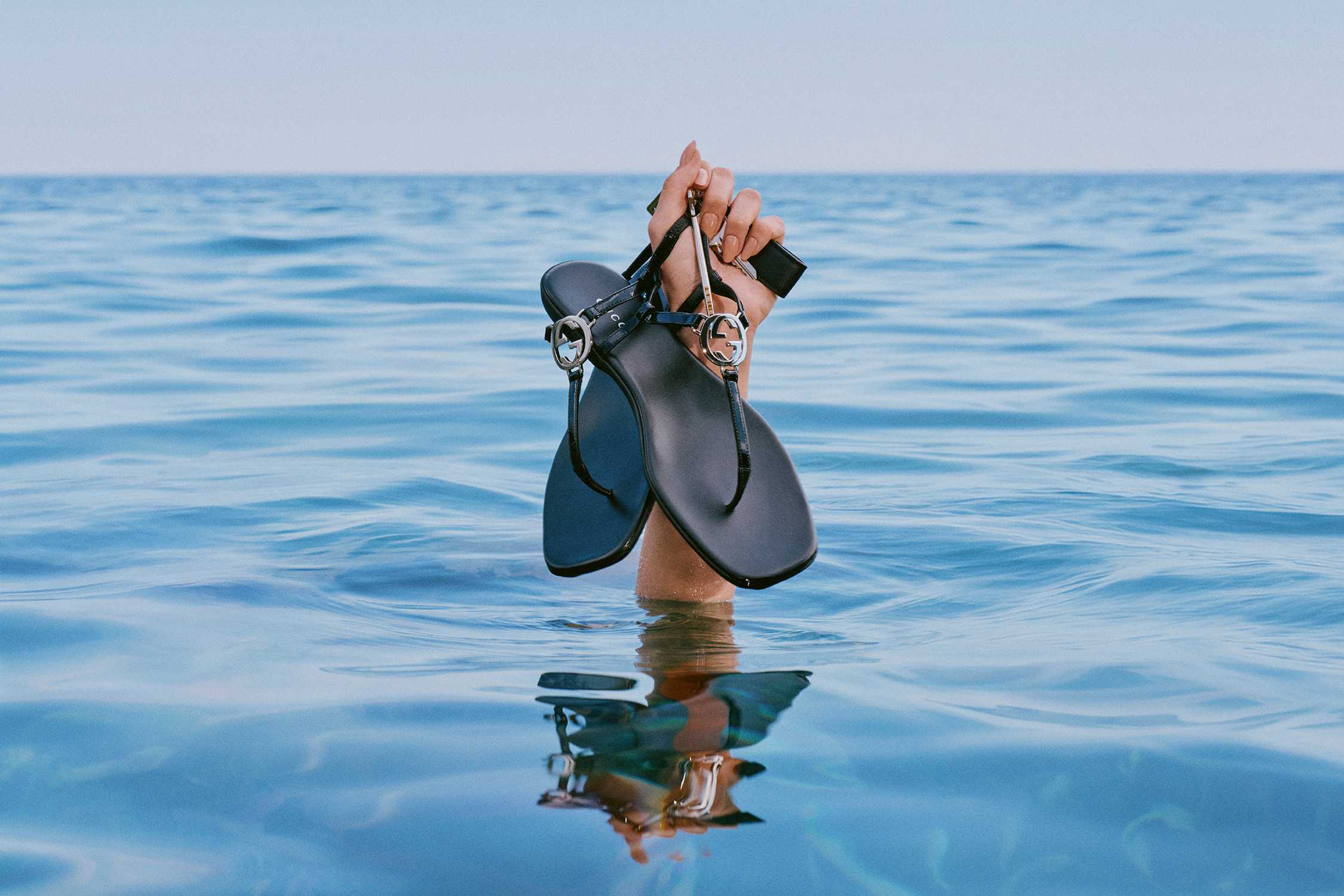 Black Gucci sandals held aloft.