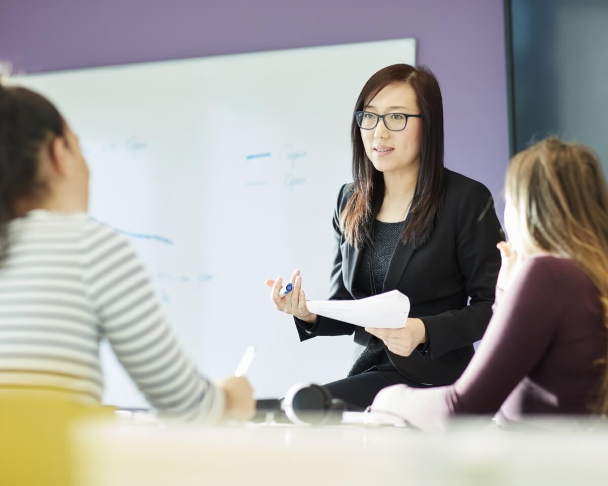 An instructor holding notes speaks to students in a classroom