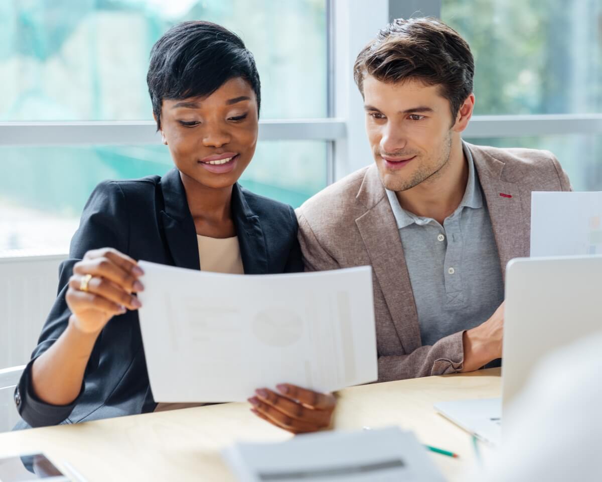 Two professionals review a document while sitting in front of an open laptop in an office