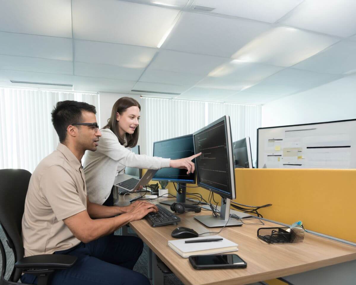 Two IT cybersecurity professionals looking at code on a monitor