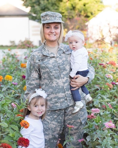 Newhart wears her U.S. Army uniform and holds her baby daughter with her toddler to her side. 