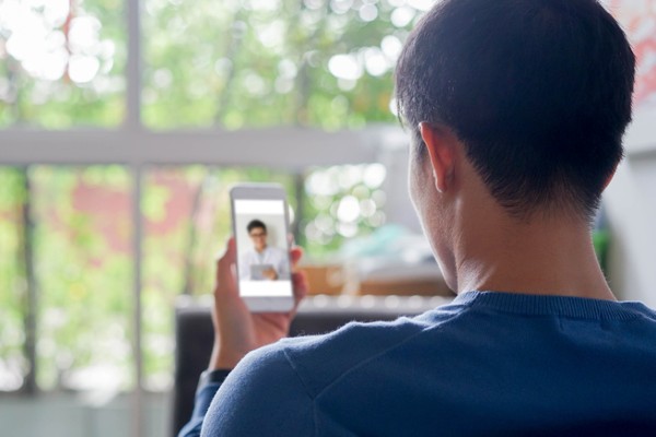 Young man using smartphone to video conference with telebehavioral health care provider