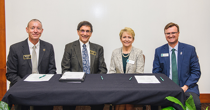 Purdue Global Provost Jon Harbor and Chancellor Frank Dooley, and Ivy Tech President Sue Ellspermann and Provost Dean McCurdy (left to right), seated at a table with three documents in front of them.