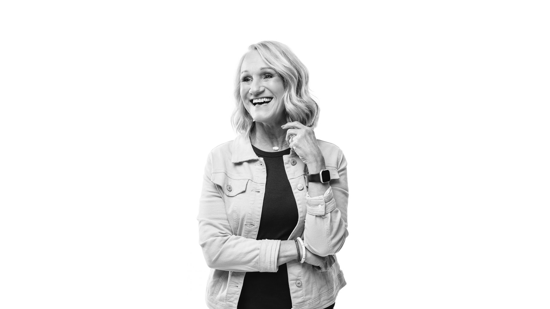 Sherry McQueary, in a black and white image, is looking toward the side and laughing, wearing a dark shirt with a light denim jacket on top.