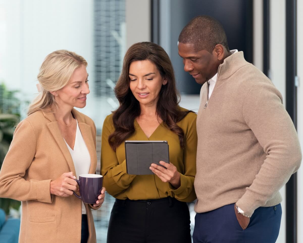 Three business professionals discuss items on a tablet in an office setting