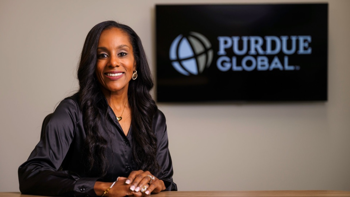 Cap: Isabelle Akins, associate dean of students for Purdue Global’s School of Business and Information Technology, says connecting students to alumni drives students’ professional and personal growth. (Purdue Global photo/Becky Robiños)

Alt: Isabelle Akins sitting at a desk with a TV screen with a Purdue Global logo behind her. 