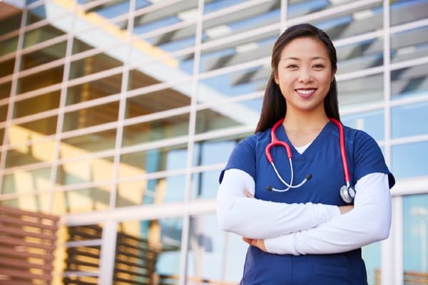 A nurse stands in front of a hospital.