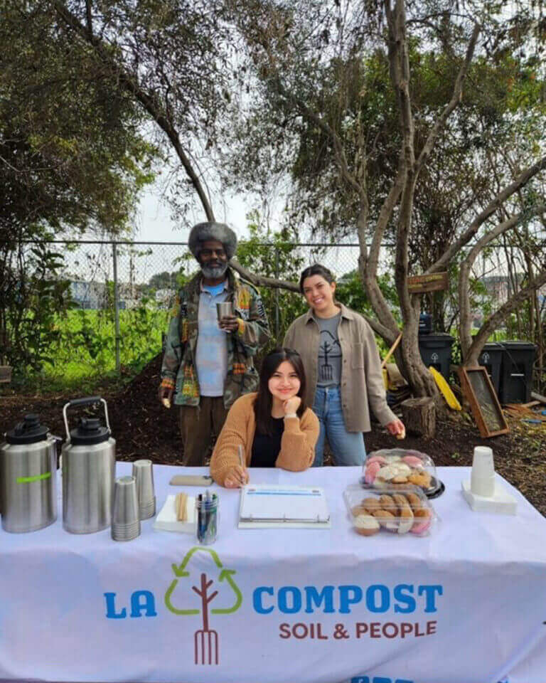 Jeshua Coronado sits with two others at a LA Compost table with refreshments