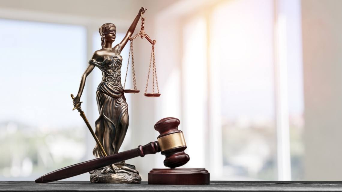 Lady Justice holding balanced scales beside a judge’s gavel.