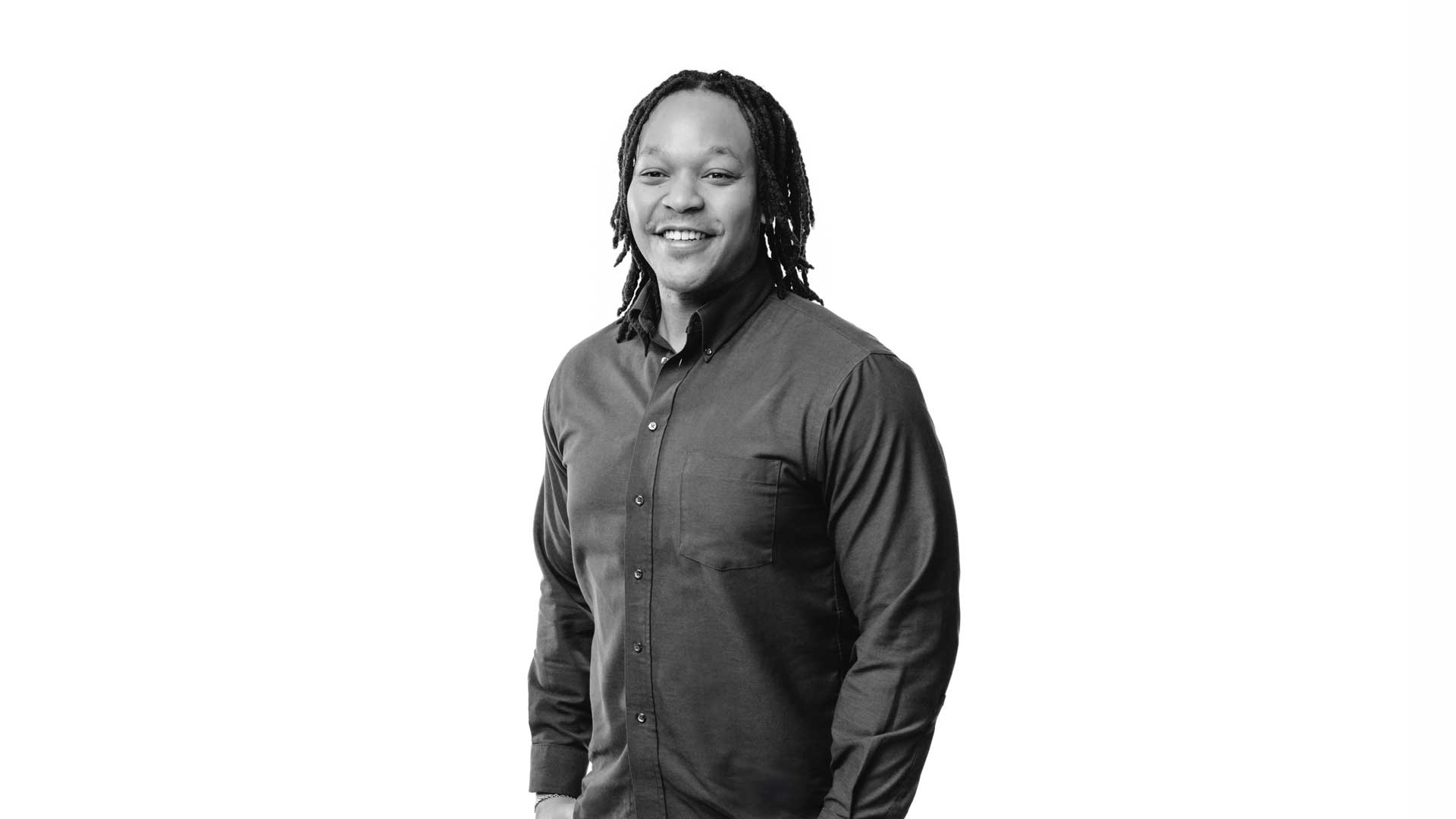 Black and white photo of TJ, smiling and wearing a dark, button-down shirt, with a white background