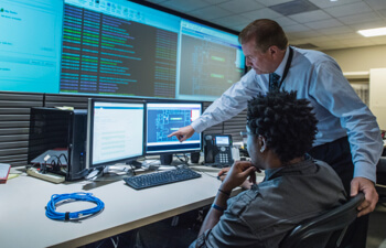 Two workers looking at code on computer monitors