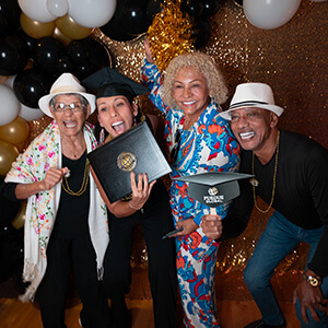 four smiling Purdue Global graduates at the Black and Gold celebration, surrounded by black and gold ballooons