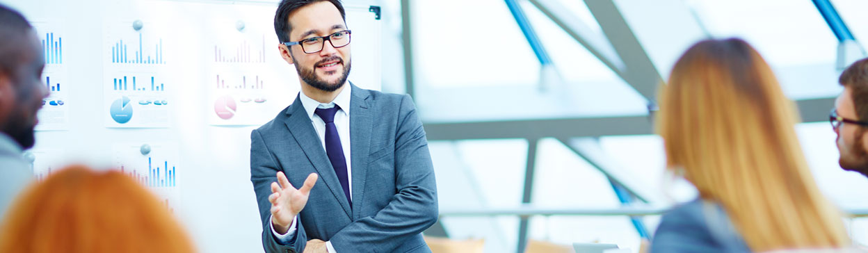 man in blue suit speaking to a room with charts behind him