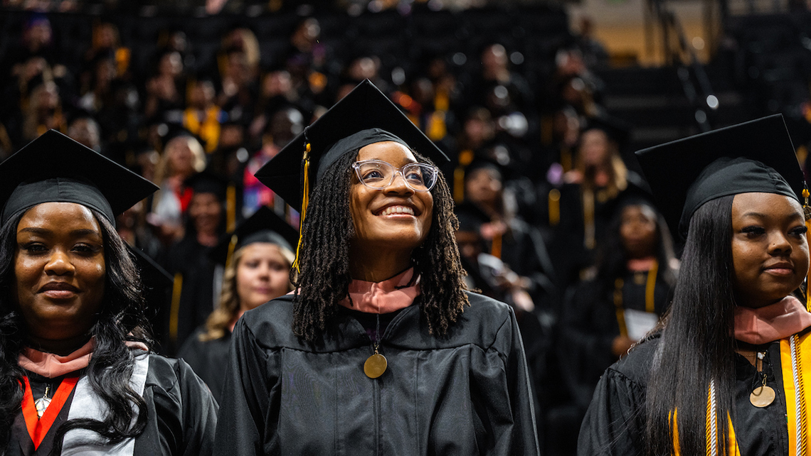 Cap: Purdue Global graduates celebrate during the October 2026 commencement ceremonies. (Purdue Global photo/Kelsey Lefever)
Alt: Three women in black graduation robes stand during a graduation ceremony.