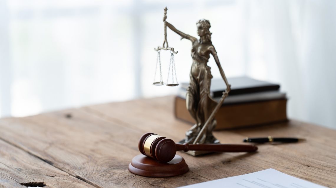 A judge’s gavel appears beside a Lady Justice statue on a desk.