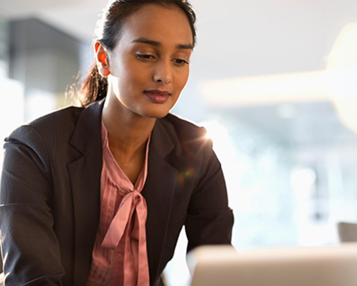 Female in professional attire sitting in a conference room working on a laptop