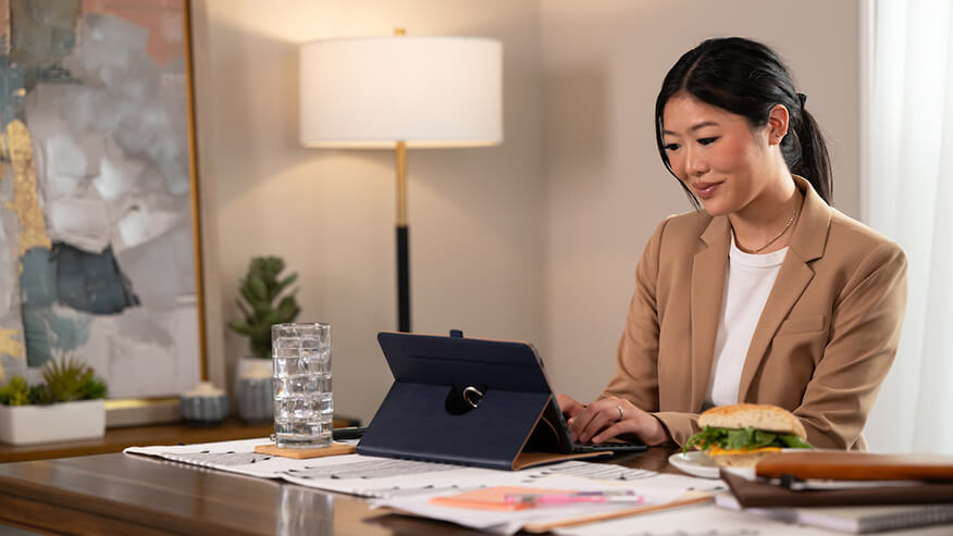 woman in a beige jacket working on a tablet in a modern office. 