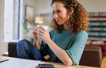 student holding a cup of coffee and looking at a monitor offscreen at home