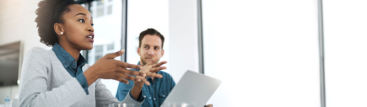 Female business professional with laptop speaking while a male colleague looks on