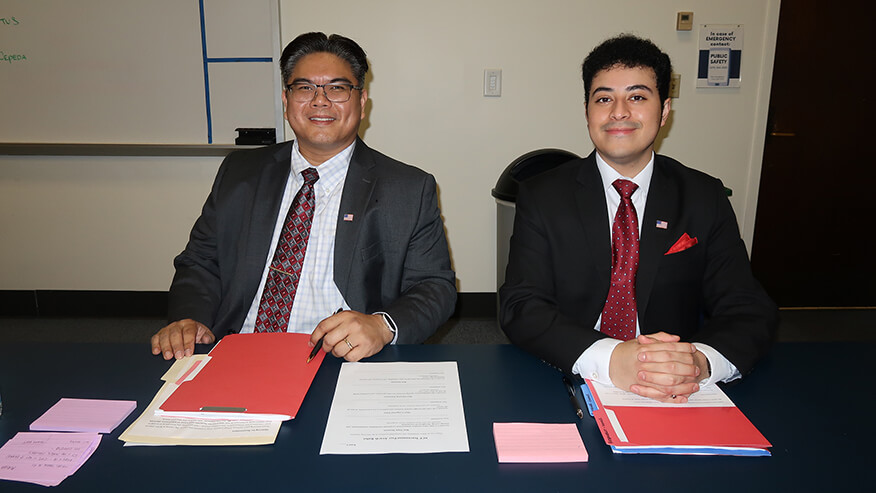 Brian Gatus, left, and Carlos Cepeda-Ojo sitting at a desk with folders of paperwork.