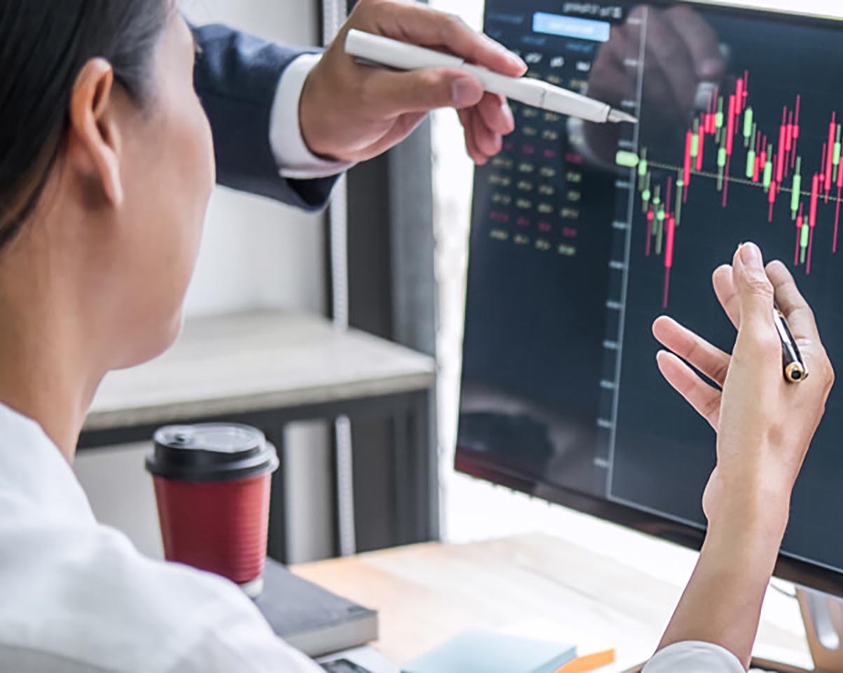 Professionals gesturing and analyzing trending chart data on a monitor, with a coffee cup nearby