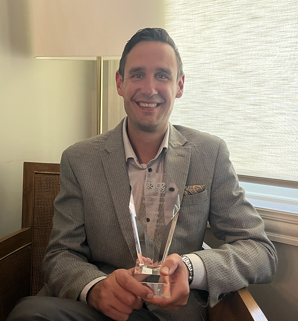 A man in a suit jacket with a clear glass award.