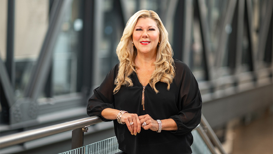 Miranda Brand in a black shirt leaning on a railing in a modern building.