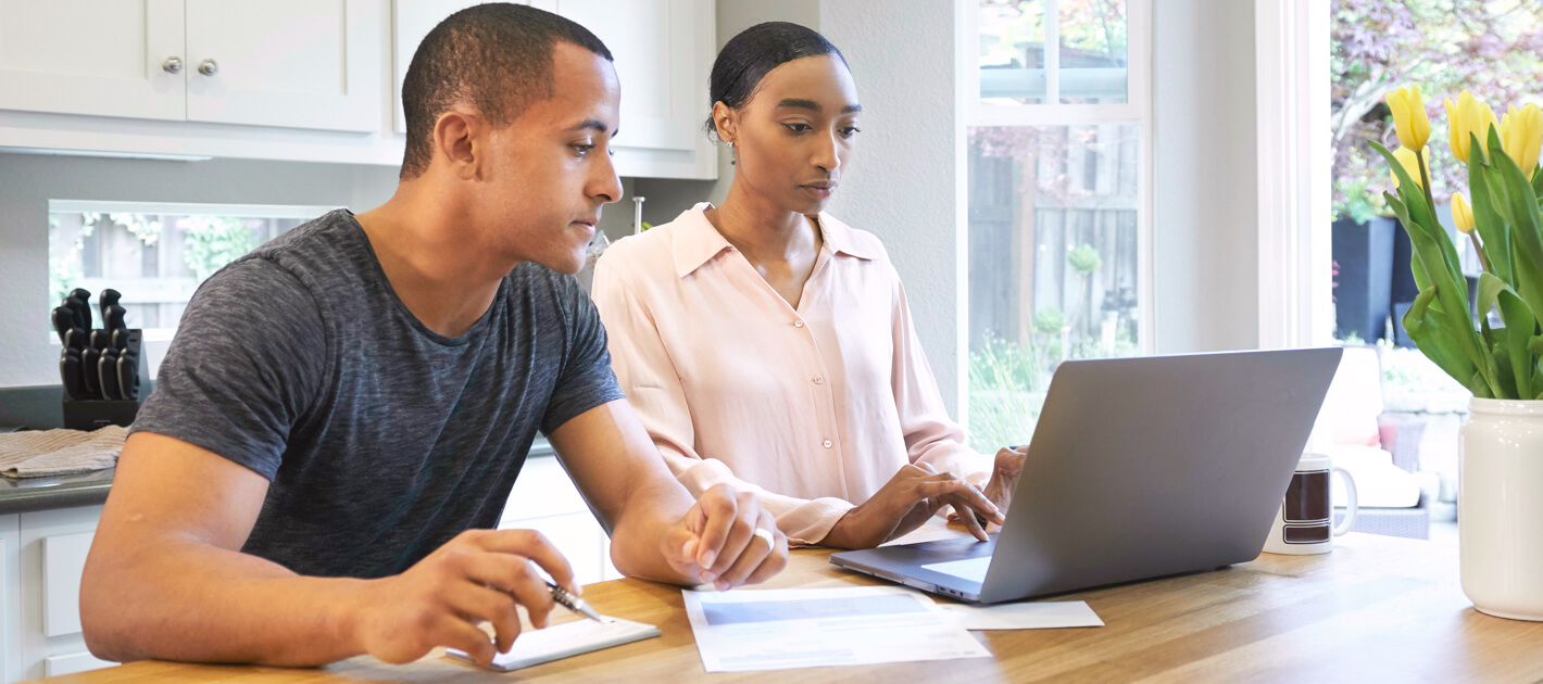 couple at home sitting at kitchen island, looking at laptop