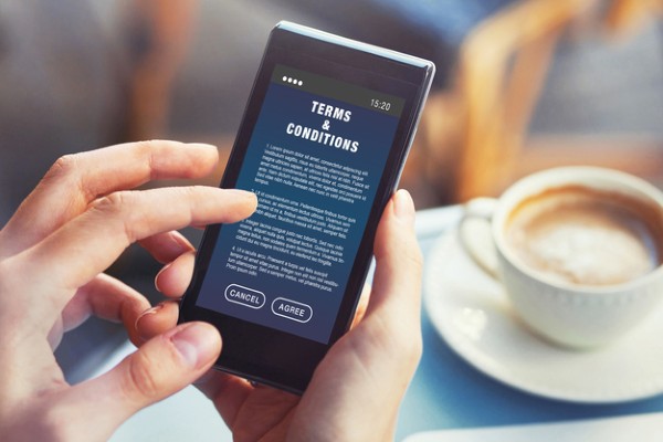 A person in a coffee shop reads terms and conditions for a website on his smartphone.