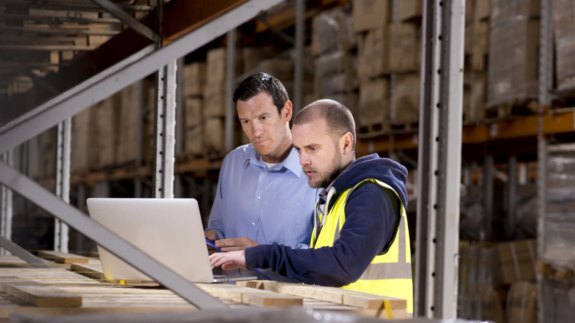 Two warehouse professionals reviewing inventory data on a laptop.