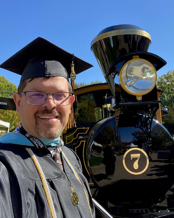 Brewer poses with the Boilermaker Special in his cap and gown at Purdue Global graduation.