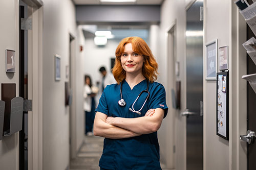Nurse in scrubs standing outside exam rooms in a medical office