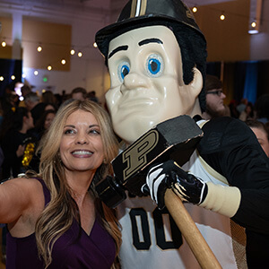 Purdue Global graduate next to Boilermaker mascot at Black and Gold celebration, with other attendees in the background
