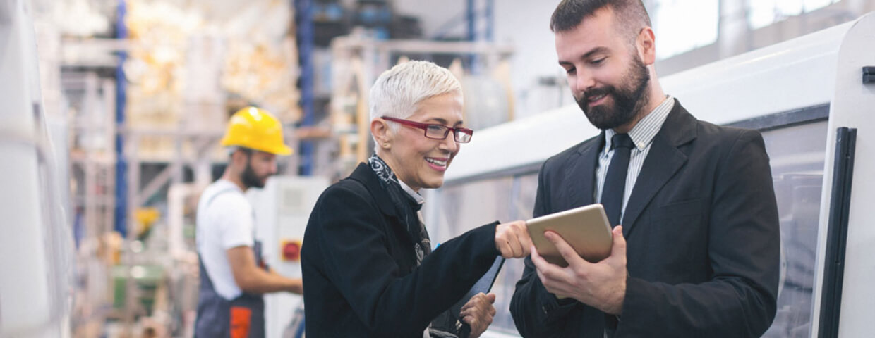 Two employees in suits looking at a tablet in a manufacturing plant