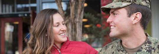 A man in military uniform smiling and talking to a woman outside a shop