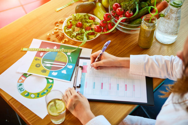 A person sits at a table with a bowl of food and writes in a book