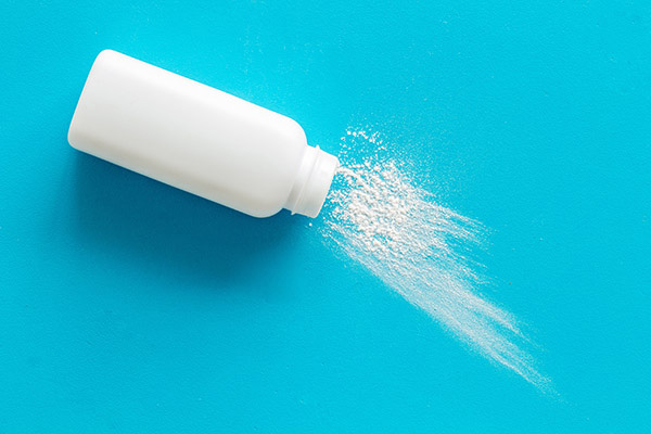 White talcum powder bottle lying on its side with powder spilled out.