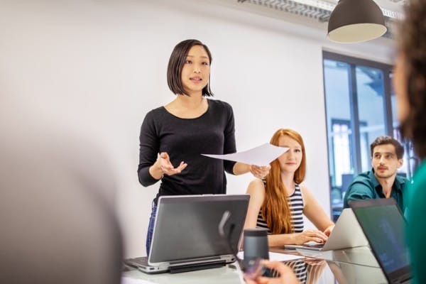 A woman stands in front of her office peers, demonstrating her communication skills