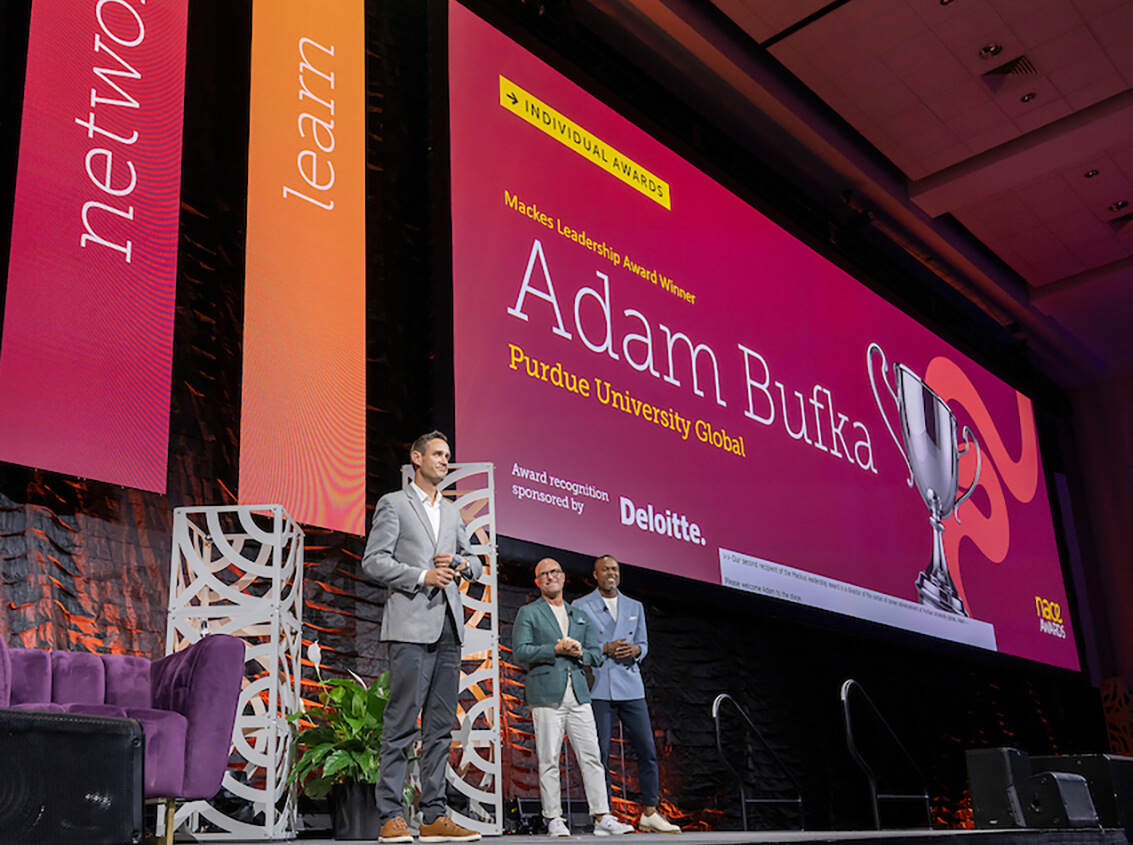 alt: A man in a gray jacket is honored onstage.